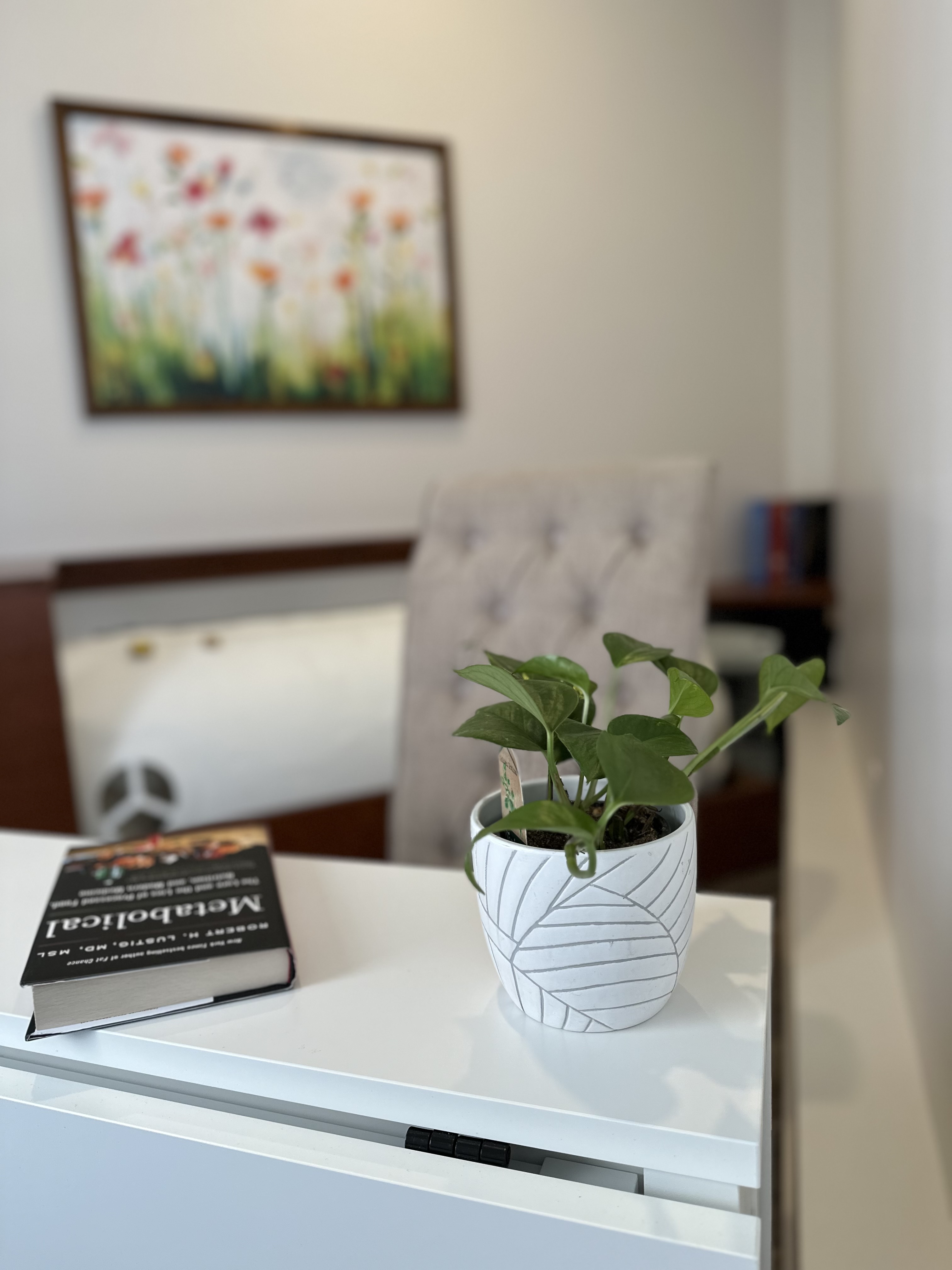 A small leafy plant on a side table beside the reading chair, with the painting and chamber softly out of focus behind.